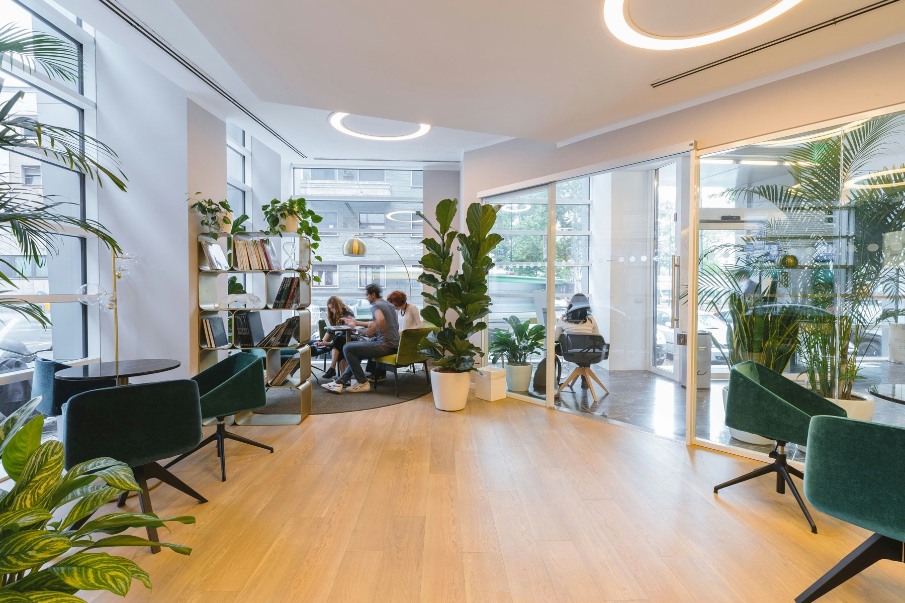 A bright workplace lounge with plants, people working at a shared table